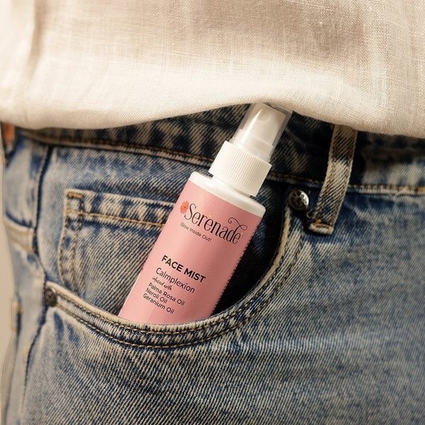 Serenade Calmplexion Face Mist in a pink bottle with floral accents, infused with Palmarosa, Neroli, and Geranium oils, tucked into a denim pocket.