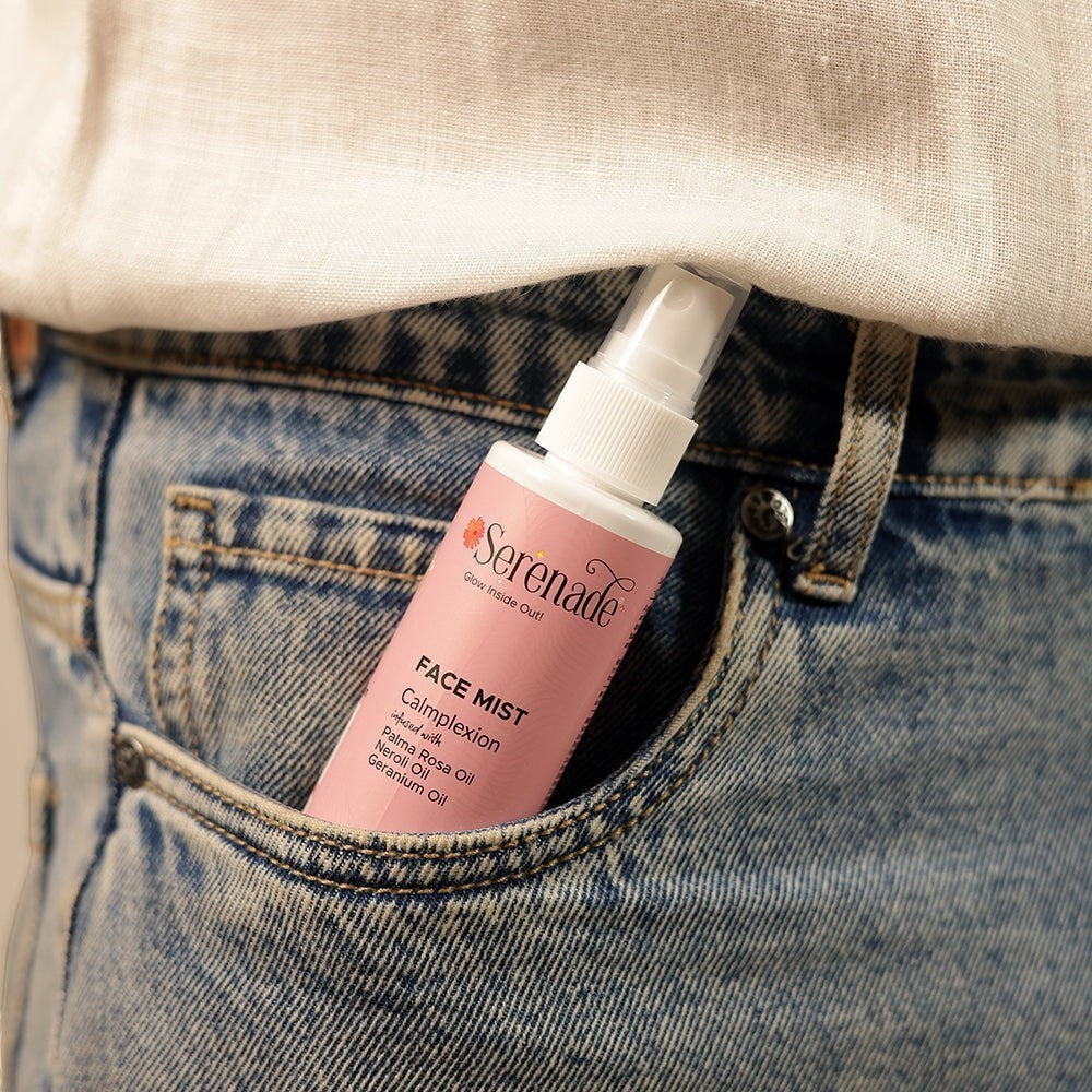Serenade Calmplexion Face Mist in a pink bottle with floral accents, infused with Palmarosa, Neroli, and Geranium oils, tucked into a denim pocket.
